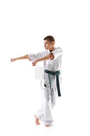 Focused martial arts student in white kimono and green belt prepares for fight, practicing isolated on white background. Concept of sport, martial arts, combat sport, healthy and active lifestyle