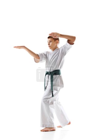 Foto de Estudiante de artes marciales enfocado en kimono blanco y cinturón verde se prepara para la lucha, practicando aislado sobre fondo blanco. Concepto de deporte, artes marciales, deporte de combate, estilo de vida saludable y activo - Imagen libre de derechos
