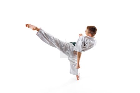 Martial arts training session capturing young athlete high kick, teen boy practicing isolated on white studio background. Concept of sport, martial arts, combat sport, healthy and active lifestyle