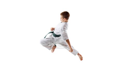 Dynamic image of teen bot, karate athlete in motion, kicking in a jump, practicing isolated on white studio background. Concept of sport, martial arts, combat sport, healthy and active lifestyle