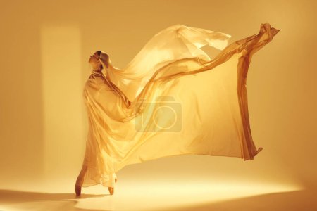 Foto de Danza de la luz. Bailarina de ballet femenina artística en vestido dorado que hace un rendimiento creativo elegante contra el fondo de color arena. Concepto de arte, danza clásica, belleza, moda, estética - Imagen libre de derechos