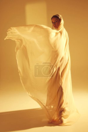 Photo for Artistic portrayal of ballerina in motion, elegant woman dancing against sand color background. Swirls of golden dream. Concept of art, classical dance, beauty and fashion, aesthetics - Royalty Free Image