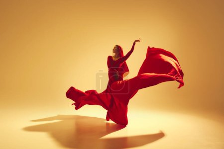 Téléchargez les photos : Performance artistique et profonde Femme, danseuse en robe rouge fluide dansant sur fond de couleur dorée. Concept d'art, danse classique, beauté et mode, esthétique - en image libre de droit