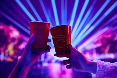 Photo for People having fun at nightclub, attending party, concert, drinking beer and clinking red cups with neon background. Concept of party, celebration, leisure activity, fun, night life - Royalty Free Image
