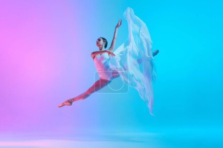Téléchargez les photos : Danseuse de ballet effectue saut divisé en mouvement avec un tissu blanc fluide dans la lumière au néon sur fond de gradient vif. Concept d'art, mouvement, fusion classique et moderne, beauté et mode. Publicité - en image libre de droit