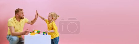 Banner. Kleiner Junge gibt High Five seinem Vater, während sie zusammen vor rosa Studiohintergrund mit Kopierraum spielen. Konzept des Tages der glücklichen Väter, Familienfeier, Elternschaft. Anzeige