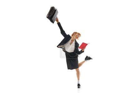 Foto de Mujer de negocios de pie en pose dinámica con maletín y mirando en el cuaderno aislado sobre fondo blanco. Multitarea y eficiencia. Concepto de negocio, estilo de vida de oficina, plazos, motivación - Imagen libre de derechos