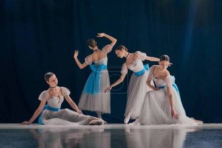 Téléchargez les photos : Quatuor de danseurs élégamment disposés, chacun présentant leur forme de ballet unique en costumes blancs fluides ornés d'arcs bleus. Concept de beauté, classique et modernité, art contemporain. Publicité - en image libre de droit