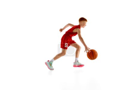 Photo for Dribbling skills. Active 11 years old boy, basketball player in red uniform in motion with ball, training isolated on white studio background. Sport, childhood, sport school, active lifestyle concept - Royalty Free Image