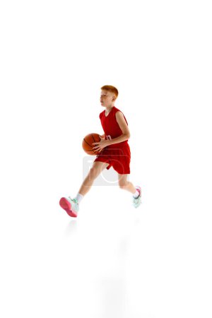 Photo for Full-length dynamic image of boy, basketball player in motion with ball, training isolated on white studio background. Concept of sport, childhood, sport school, active lifestyle - Royalty Free Image