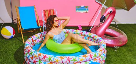 Foto de Young beautiful woman in striped retro swimsuit relaxes in inflatable pool with neon- green float ring. Summer. Concept of pop art, remote work, travelling, party, recreation, lifestyle, style. - Imagen libre de derechos