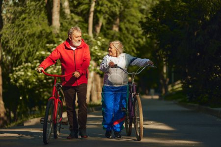 Photo for Senior couple, smiling, happy man and woman, joyfully bicycles through park, showing enduring spirit and love for outdoor activities. Concept of sport, aging, active and healthy lifestyle, health care - Royalty Free Image