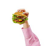 Woman holding juicy burger with two all-beef patties, melted cheese, crisp lettuce, tomato, onion, isolated on white background. Concept of food, cooking, cuisine, taste. Copy space for ad