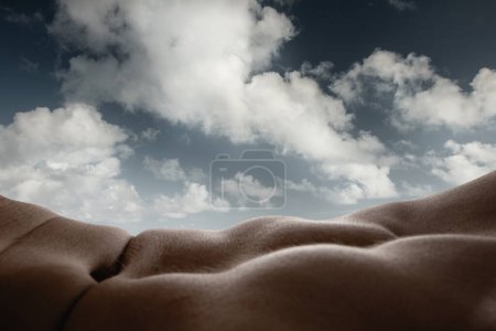 Beauty of cloud formations and human body curves. Close-up of tanned male muscular body forming natural landscape with cloudy sky on background. Concept of body aesthetics, nature and beauty of human