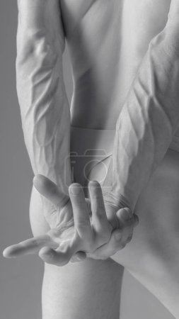 Image en noir et blanc du dos masculin musclé avec les bras croisés derrière, soulignant les veines et les muscles définis, mettant l'accent sur la texture et la forme. Concept d'esthétique corporelle, nature et beauté de l'homme.