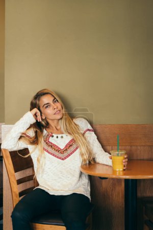 Foto de Mujer joven sola sentada en una mesa sola tomando una copa. - Imagen libre de derechos