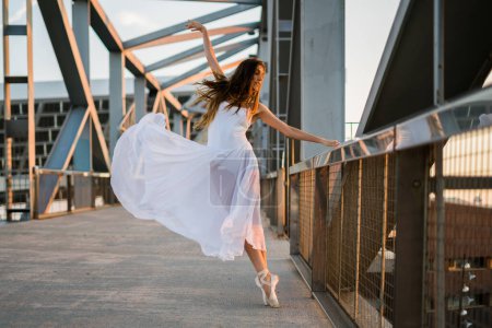 Foto de Bailarina joven adulta bailando en un puente con vestido blanco. - Imagen libre de derechos