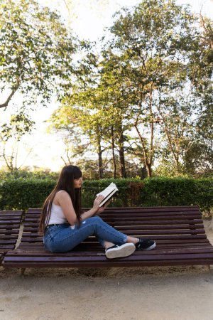 Foto de Joven asiática con flecos leyendo un libro negro en las calles de Barcelona con luz natural del sol - Imagen libre de derechos