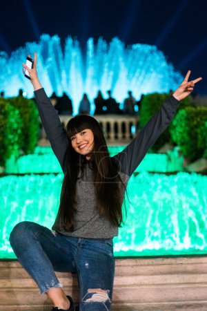 Photo for Pretty asian european girl having fun in Barcelona, in the party of the Monjuic font lights. She wears modern clothes and her hair is brunette with a fringe haircut - Royalty Free Image