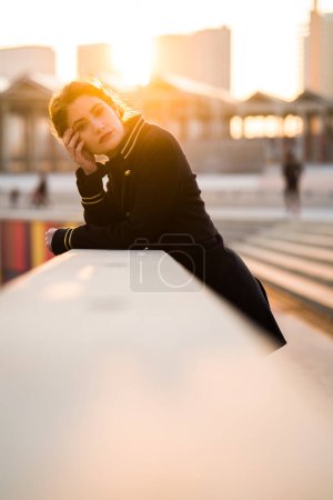 Téléchargez les photos : Jeune femme portant une veste noire et dorée penchée sur le balcon regardant la caméra - en image libre de droit