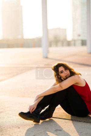 Foto de Mujer adulta joven con un top rojo sentado en el suelo al aire libre. - Imagen libre de derechos