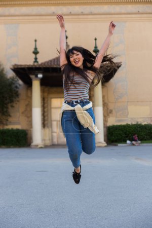 Photo for Asian european young woman jumping in Montjuic, Spain. She is brunette, with a fringe haircut and wears summer clothes - Royalty Free Image