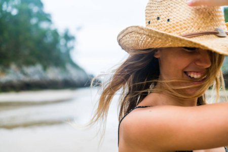 Téléchargez les photos : Jeune fille blonde adulte portant un chapeau de paille et robe courte marchant seule sur la plage en s'amusant. - en image libre de droit