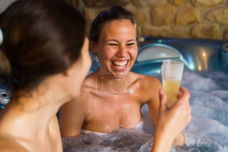 Téléchargez les photos : Deux couples féminins dans un bain bouillonnant portant un toast au champagne. - en image libre de droit