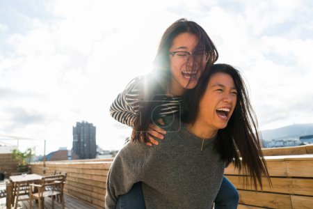 Foto de Dos chicas jóvenes chinas en ropa casual divirtiéndose juntas en la terraza. - Imagen libre de derechos