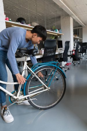 Photo for Young Asian man fixing bicycle in office building. - Royalty Free Image