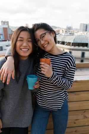 Foto de Jóvenes chicas alegres abrazando y mirando a la cámara mientras sostiene bocadillos y café. - Imagen libre de derechos