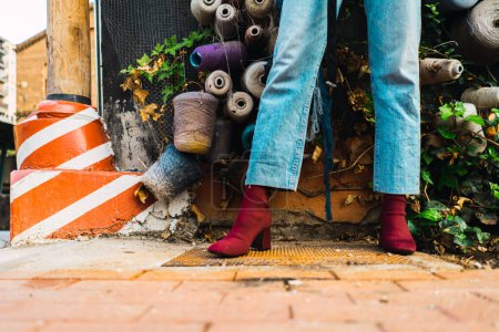 Foto de Primer plano en un modelo pies con un vaquero jean y botas rojas de pie contra una pared con hilo de coser decoración. - Imagen libre de derechos