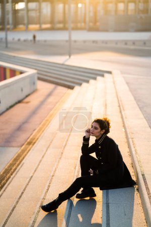 Téléchargez les photos : Adulte jeune femme portant tout noir assis sur les escaliers à l'extérieur - en image libre de droit