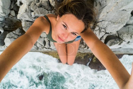 Téléchargez les photos : Tourné d'en haut d'une jeune femme blonde assise sur le bord d'une falaise regardant vers la caméra. - en image libre de droit