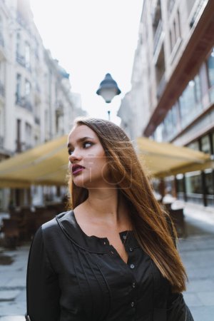 Photo for Young adult woman looking away from camera standing outside in a city center. - Royalty Free Image