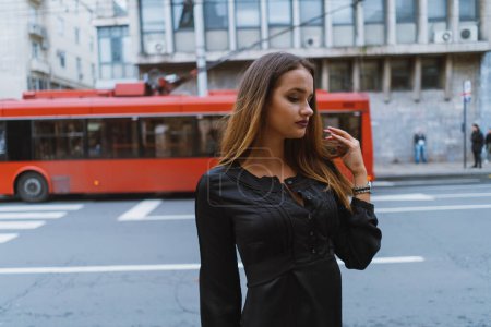 Téléchargez les photos : Jeune femme portant tout noir regardant loin de la caméra avec un bus rouge passant par - en image libre de droit