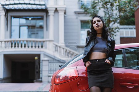 Foto de Joven mujer caucásica adulta vistiendo todo negro mirando a la cámara acostada en un coche rojo. - Imagen libre de derechos