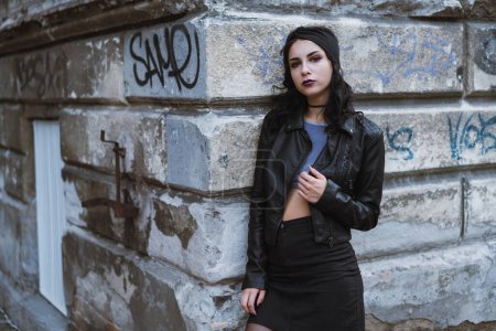 Téléchargez les photos : Jeune femme caucasienne adulte portant tout noir regardant la caméra couchée sur un mur de briques avec des graffitis - en image libre de droit