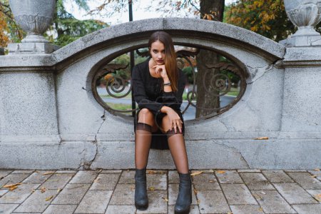 Téléchargez les photos : Jeune femme portant tout noir assis dehors regardant la caméra d'une manière sensuelle. - en image libre de droit