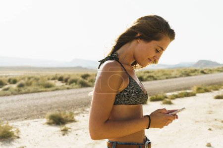 Téléchargez les photos : Shot of a young woman in a desert area browsing her cellphone - en image libre de droit