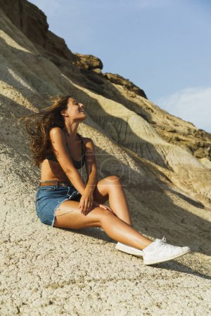 Foto de Young adult outdoors siting on a rock in an arid landscape. - Imagen libre de derechos
