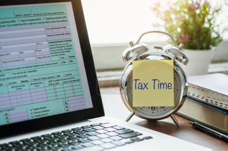 Téléchargez les photos : Tax Concept. tax time post-it on the alarm clock and Individual income tax return form online from home - en image libre de droit