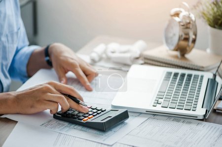 Foto de Young man holding pen working on calculator to calculate business data, taxes, bills payment, Start up counting finance.accounting, statistics, and analytic research concept - Imagen libre de derechos