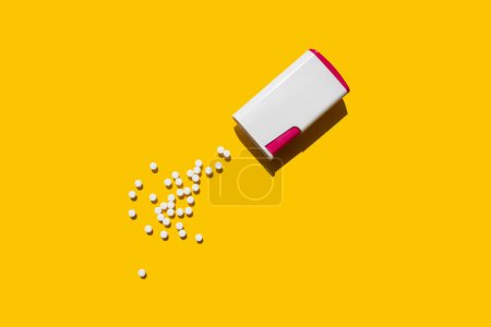 Foto de Envase edulcorante junto al cual se encuentran tabletas dulces sobre un fondo amarillo - Imagen libre de derechos