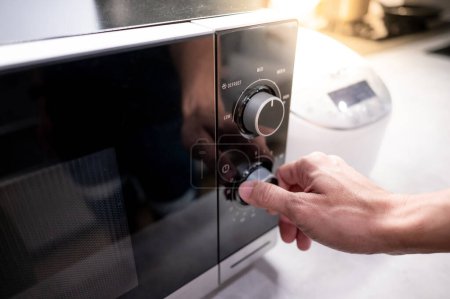 Téléchargez les photos : Main mâle tournant bouton de température du micro-ondes moderne dans la salle d'exposition de la cuisine. Acheter un appareil de cuisine pour la cuisine domestique. Concept d'amélioration résidentielle - en image libre de droit