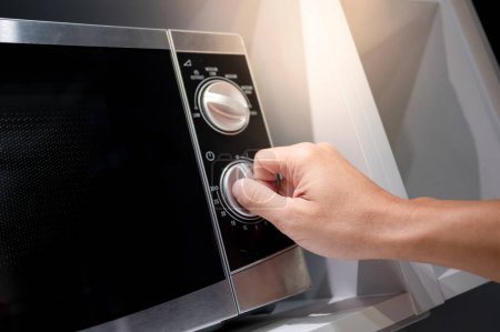 Téléchargez les photos : Main mâle tournant bouton de température du micro-ondes moderne dans la salle d'exposition de la cuisine. Acheter un appareil de cuisine pour la cuisine domestique. Concept d'amélioration résidentielle - en image libre de droit