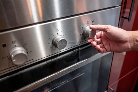 Téléchargez les photos : Main mâle tournant bouton de température du four moderne dans le showroom de la cuisine. Acheter un appareil de cuisine pour la cuisine domestique. Concept d'amélioration résidentielle - en image libre de droit