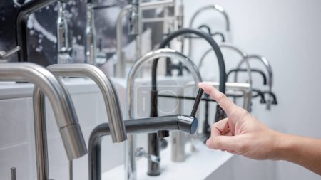 Male hand choosing modern black water tap in furniture store. Home improvement for domestic kitchen.