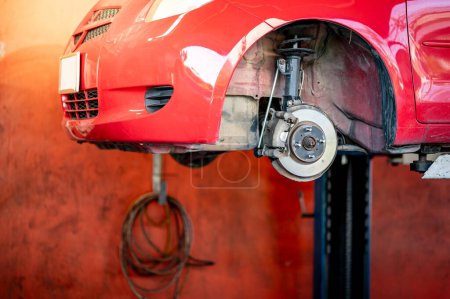 Foto de Componente de freno de disco del coche rojo en elevación hidráulica en taller de reparación de automóviles. Cambio de neumático o la fijación de suspensión del coche en el garaje. Sistema de frenado y amortiguador de mantenimiento. Ingeniería mecánica automotriz - Imagen libre de derechos