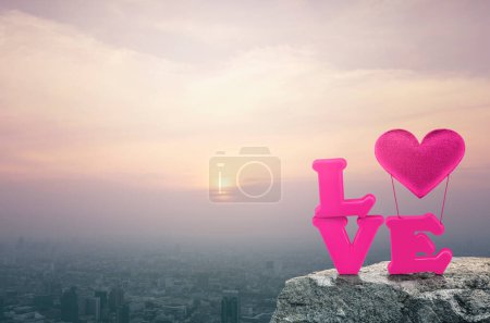 Pink love alphabet and fabric heart balloon on rock mountain over aerial view of cityscape at sunset, vintage style, Valentines day concept